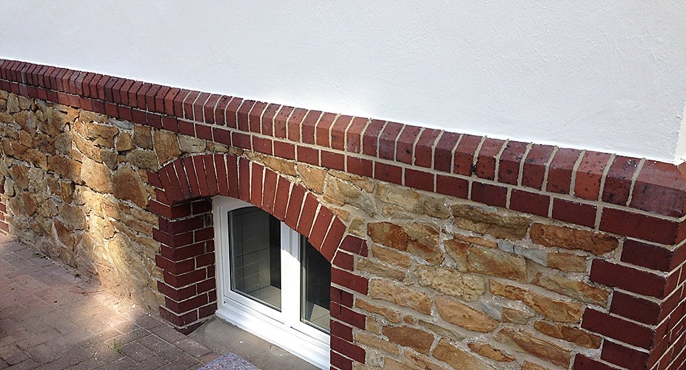 Sanierte Bruchsteinmauer aus Sandstein mit Ziegelbögen am rückseitigen Sockel der Villa Emmilio