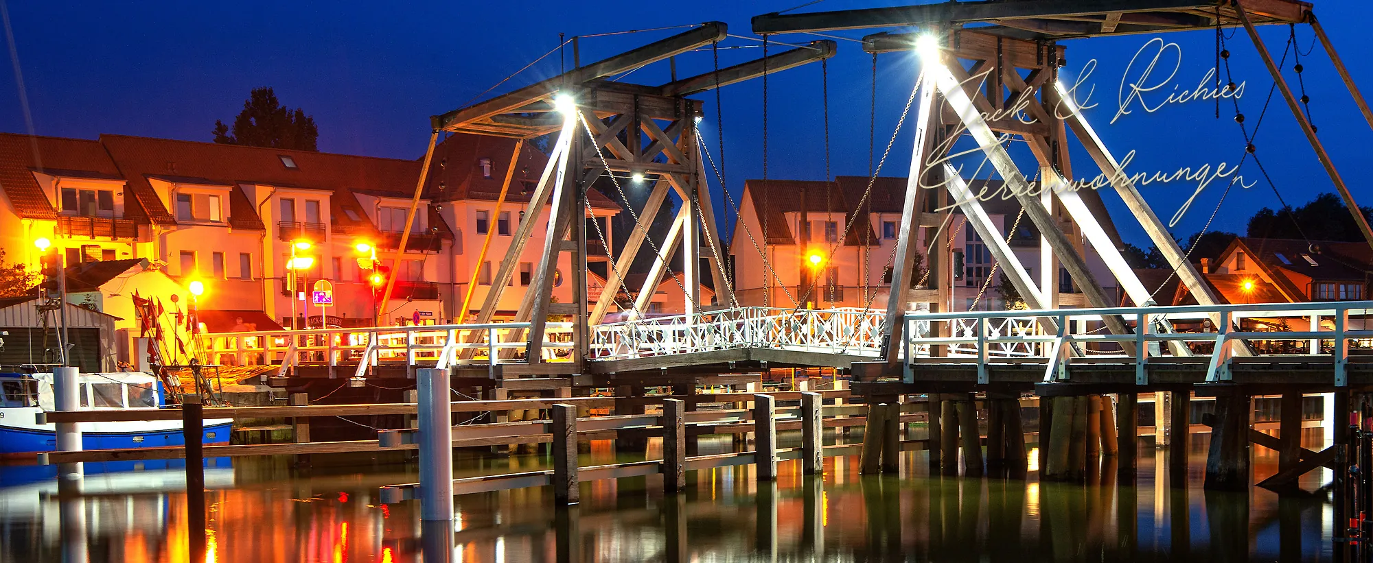 Die beleuchtete Wiecker Klappbrücke bei Nacht vor dem Haus von Jack & Richie's